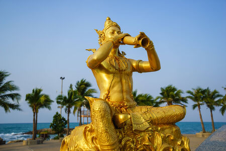 golden statue of Phra Aphai Mani blowing his pipe by the seaの写真素材