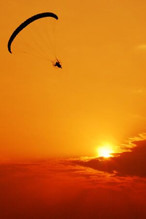 Silhouette image of a paramotor flying on sunset background.の写真素材