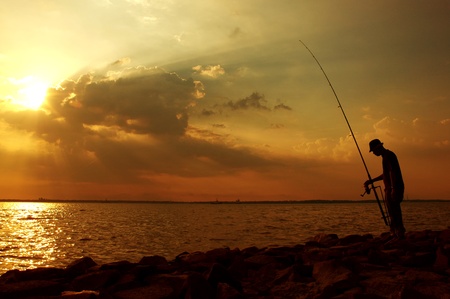 Silhouette image of a fisherman fishing at sunset.の写真素材