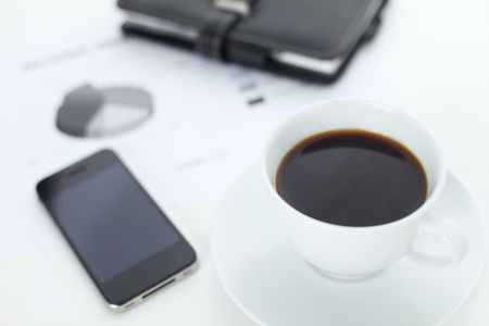 Business concept, coffee cup with phone and notebook showing statisticsの写真素材