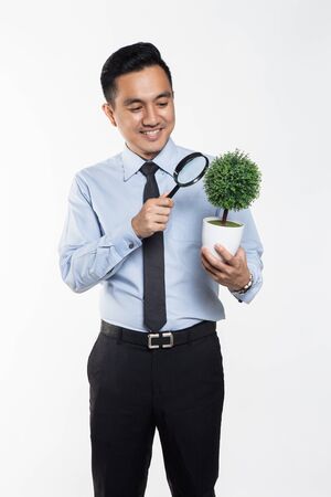 Man in office wear holding a potted plant while magnifying on itの写真素材
