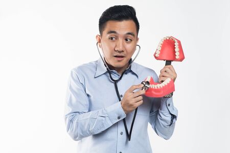Asian man holding a stethoscope examining teeth.
