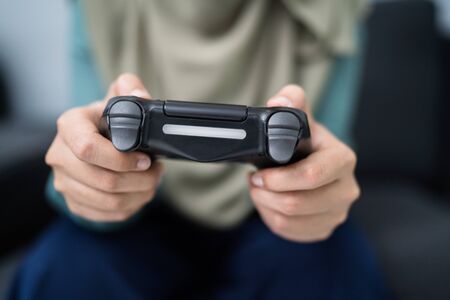 Beautiful muslim woman playing console games at her couch.