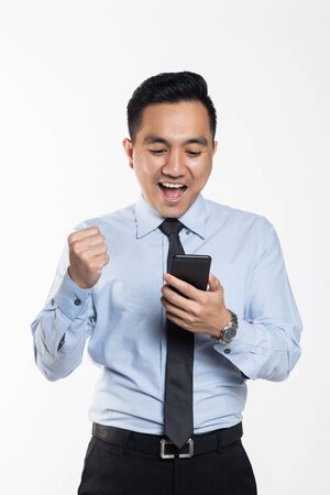 Asian man in office wear looking at his handphone with being success expressionの写真素材