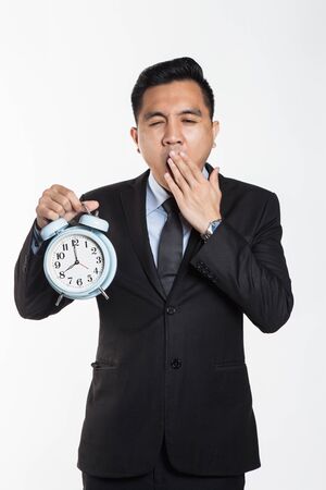 Asian business man with alarm clock with sleepy expressionの写真素材
