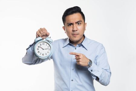Asian man pointing at an alarm clock with angry expressionの写真素材