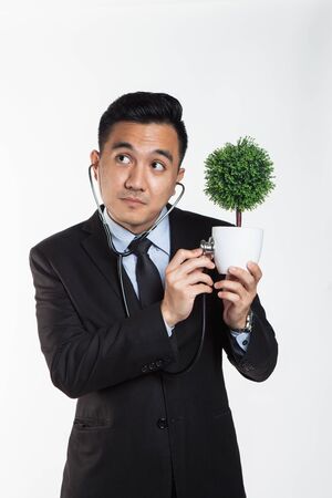 Man in suit checking a potted plant with a stethoscopeの写真素材