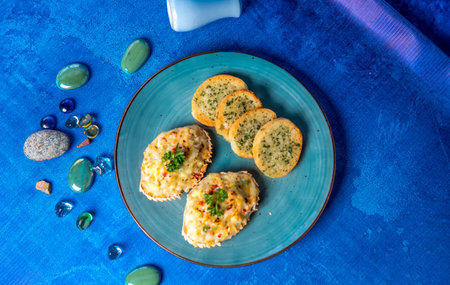 A top view of baked appetizers on a turquoise plate, garnished with fresh herbs, served on a vibrant blue background with decorative stones.の写真素材