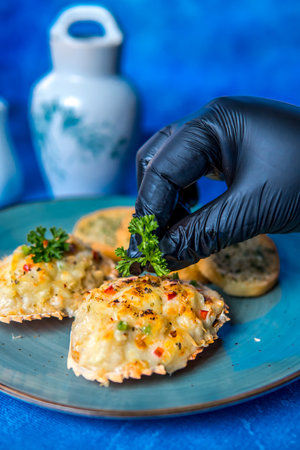 Chef's hand in a black glove holding a piece of bread with cheese and parsleyの写真素材