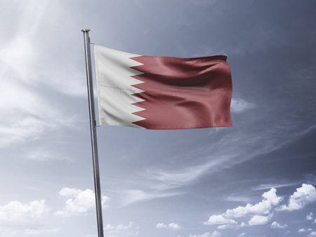 Qatar flag waving in the wind against a blue sky with cloudsの写真素材