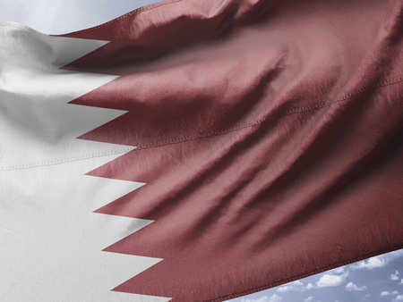 Qatar flag waving in the wind against a blue sky with cloudsの写真素材