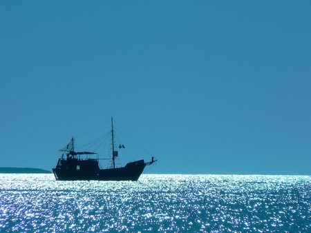 Small ship in sun glare. Solar flares on the water and silhuette of a two-masted boat.の写真素材