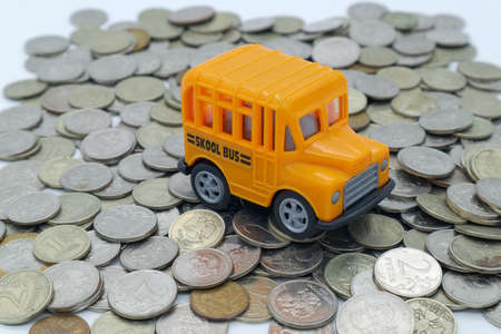 A toy school bus on a slide of metal coins. White background. Subject shooting