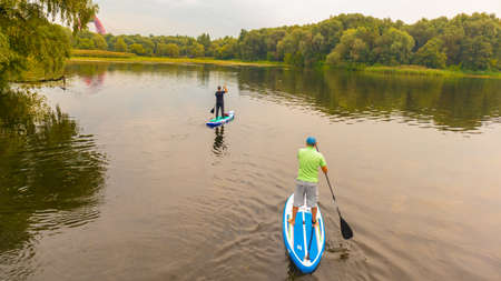 An elderly woman on a surfboard swims on the lake. Autumn.