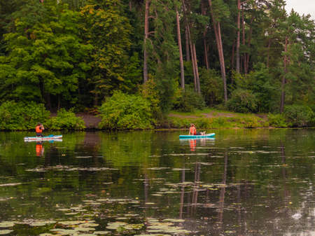 Two women relax on a forest lake swimming on surfboards