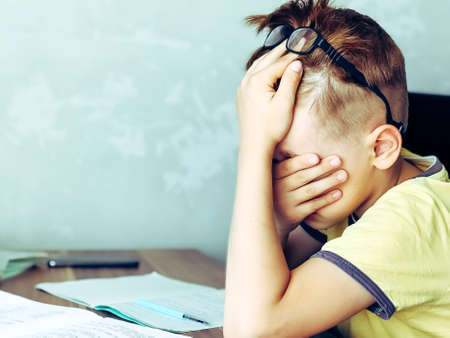 A 9 year old boy is teaching lessons. Homework and home schooling. Stress and fatigue from exercise.の写真素材