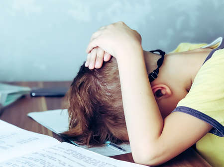 A 9 year old boy is teaching lessons. Homework and home schooling. Stress and fatigue from exercise.の写真素材