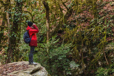Girl in red jacket with backpack walking in the forest and taking picturesの写真素材