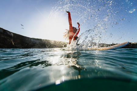 woman sitting on the surfboard in the water and doing splashes