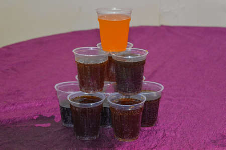 A pyramid of cold drink in plastic glasses isolated on purple table.
