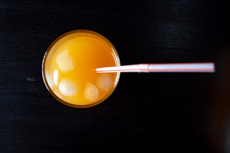 Orange juice with ice cubes in a glass on black background, top view