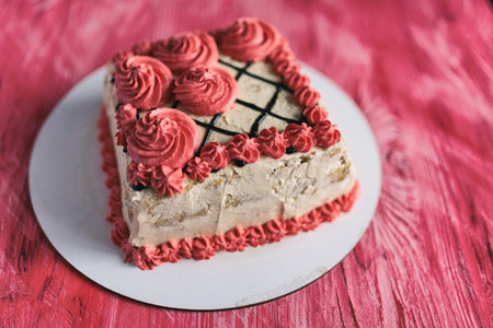 A piece of cake with cream and chocolate on a pink wooden background