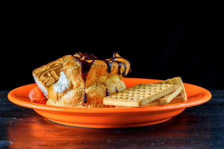 Waffle with chocolate sauce and cookies on a plate on black background