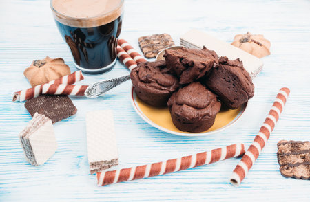 Chocolate muffins and coffee in a glass mug are photographed on a light wooden background.の写真素材