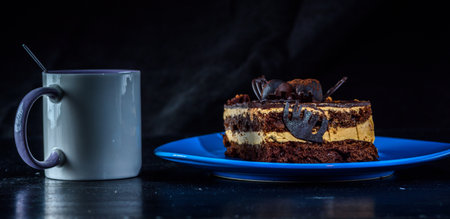 Cake on a blue ceramic plate on a black background, next to a cup of coffee.の写真素材