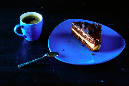 A piece of chocolate cake on a blue plate. Near a cup of coffee. All on a black wooden background.の写真素材