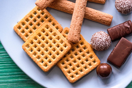 Shortbread cookies and chocolates on a turquoise plate, standing on a green wooden background.