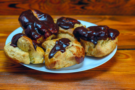 Profiteroles with chocolate on a plate on a wooden background.
