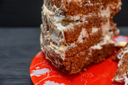 Homemade cake with cream on a red plate on a dark wooden background
