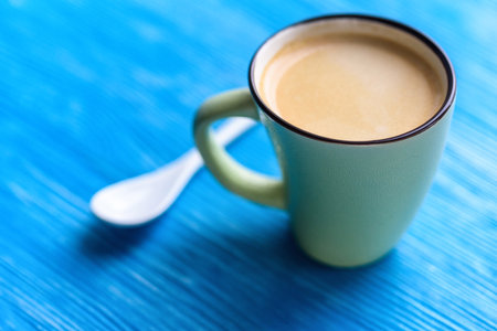 A cup of coffee on a turquoise background, next to a coffee spoon.の写真素材