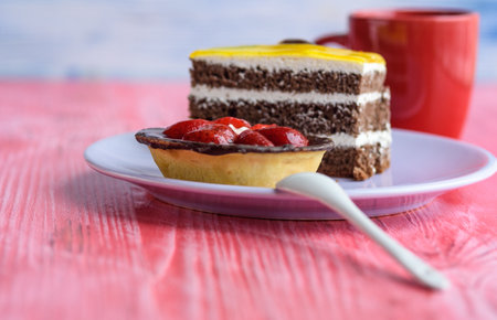 A cupcake with strawberries and a puffy biscuit cake on a plate, next to coffee in a cup.