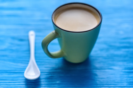 A cup of coffee on a turquoise background, next to a coffee spoon.の写真素材