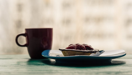 A cupcake with a strawberry, next to coffee in a red cup, photographed on a wooden background.の写真素材