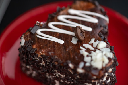 A delicious heart-shaped cake sprinkled with pieces of chocolate lies on a red plate. Photographed close-up on a wooden background.の写真素材