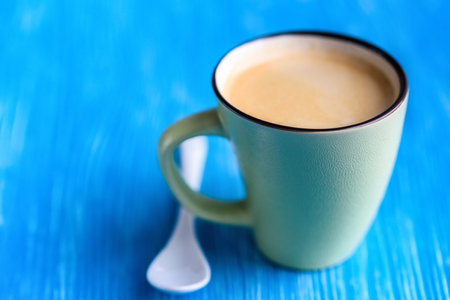 A cup of coffee on a turquoise background, next to a coffee spoon.の写真素材