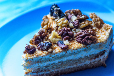 Walnut sponge cake slice photographed close-up on a blue plate, on wooden background.の写真素材