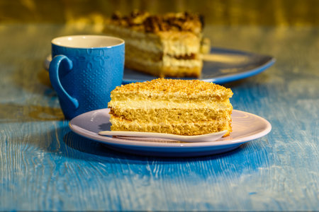 Sponge cake with walnuts, near a cup of coffee on wooden background.