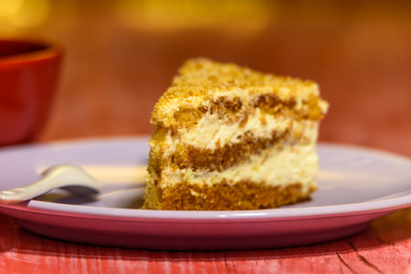 A slice of sponge cake with walnuts, next to a cup of coffee.
