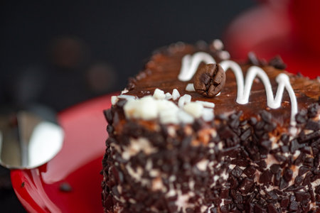 A delicious heart-shaped cake sprinkled with pieces of chocolate lies on a red plate. Photographed close-up on a wooden background.の写真素材