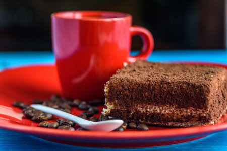 Tiramisu cake on a red plate, near a cup of coffee.