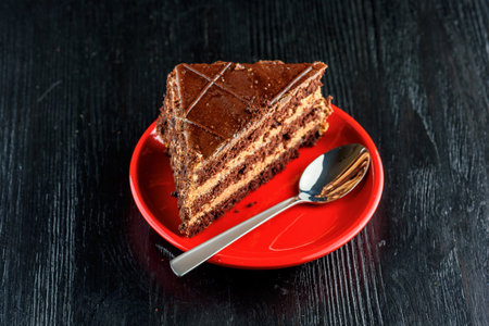 Piece of chocolate cake on red plate with spoon on black wooden tableの写真素材