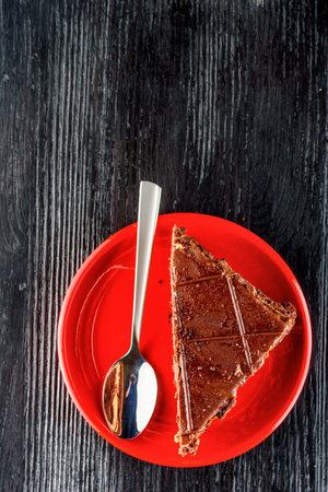 Piece of chocolate cake on red plate with spoon on wooden backgroundの写真素材