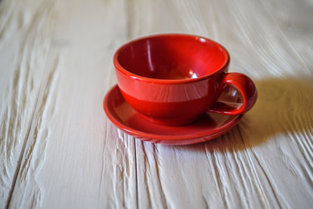 a red mug with a saucer on a white wooden background.の写真素材