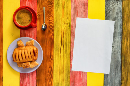 puff pastry with jam on a red plate and coffee mug on a multi-colored wooden backgroundの写真素材