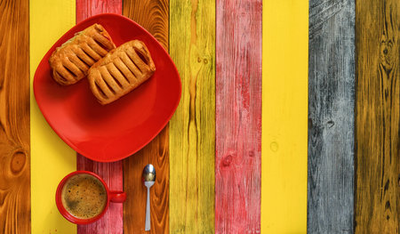 puff pastry with jam on a red plate and coffee mug on a multi-colored wooden backgroundの写真素材
