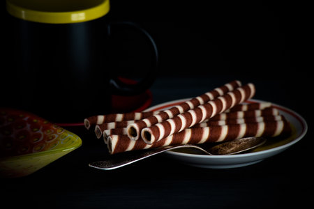 Chocolate wafer rolls with chocolate chips on a black background.の写真素材